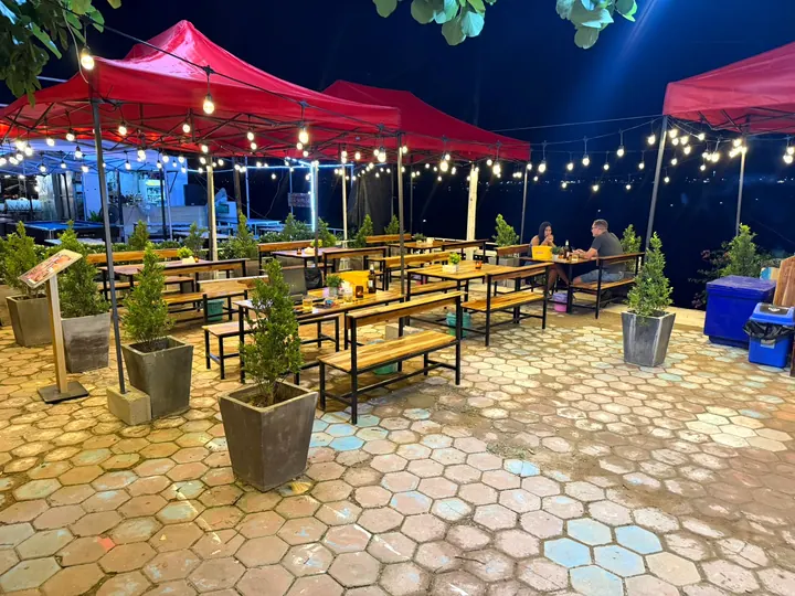 Wooden tables and benches under red canopies and string lights on the Habibi Eatery terrace
